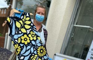 Primrose Hospice charity shop manager holding dress while wearing PPE