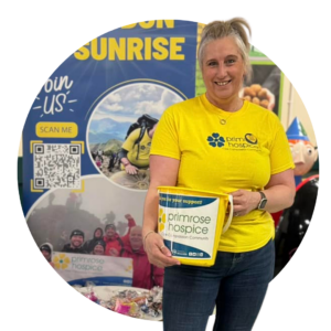 A woman standing in a yellow tshirt with a primrose hospice charity collecting bucket