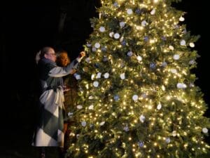 Two women hanging remembrance baubles on a lit up christmas tree.