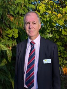 A man in a shirt and tie, stood outside.